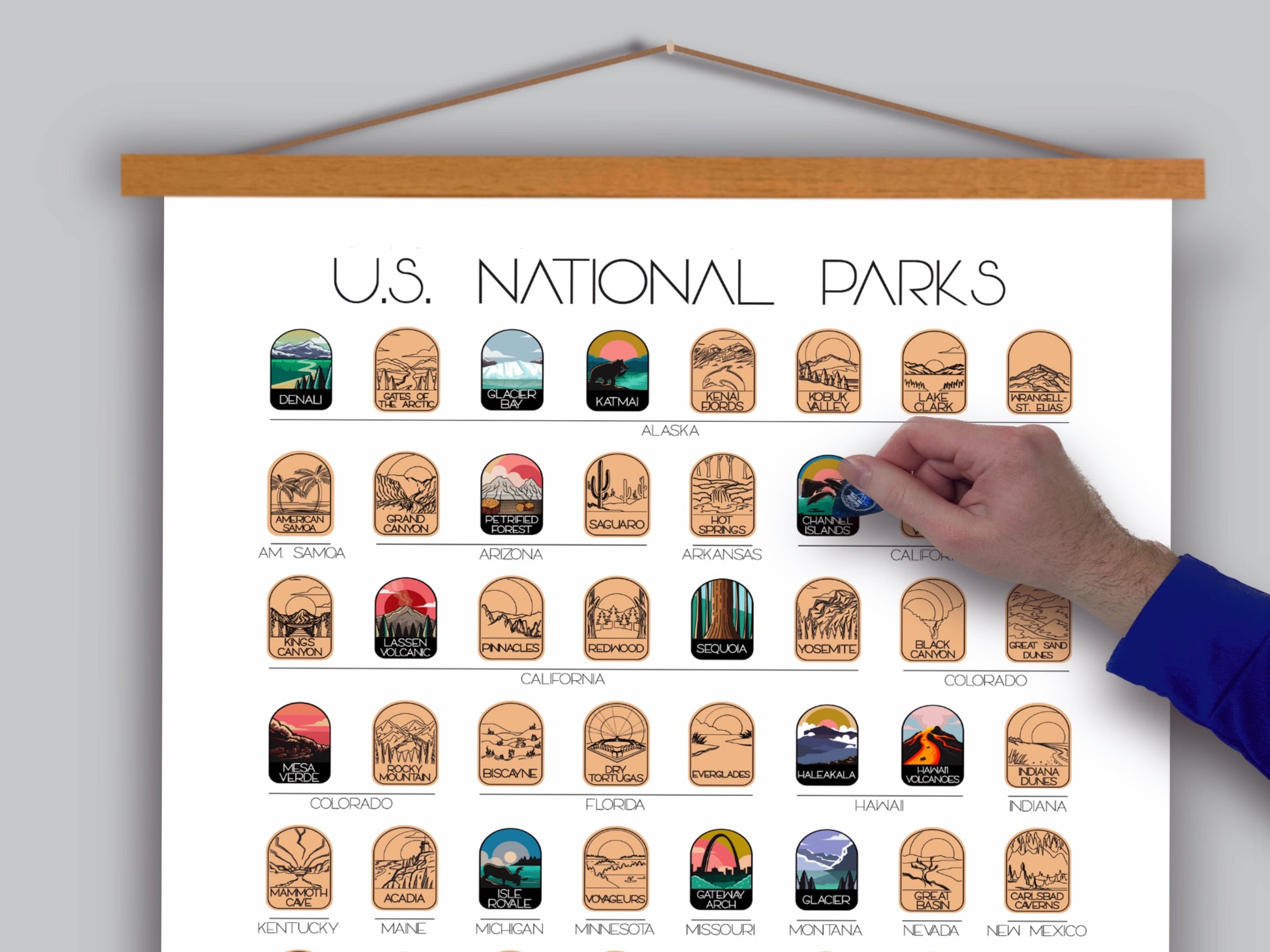 63 National Park scratch off poster, Has a white background with colorful icons for each park. Scratch off a gold layer to reveal artwork. Hanging on a wooden frame.