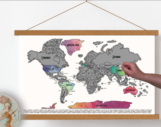 World Map scratch off poster. Has a white background with colorful watercolors under a silver scratch off a layer. Hanging on a wooden frame.