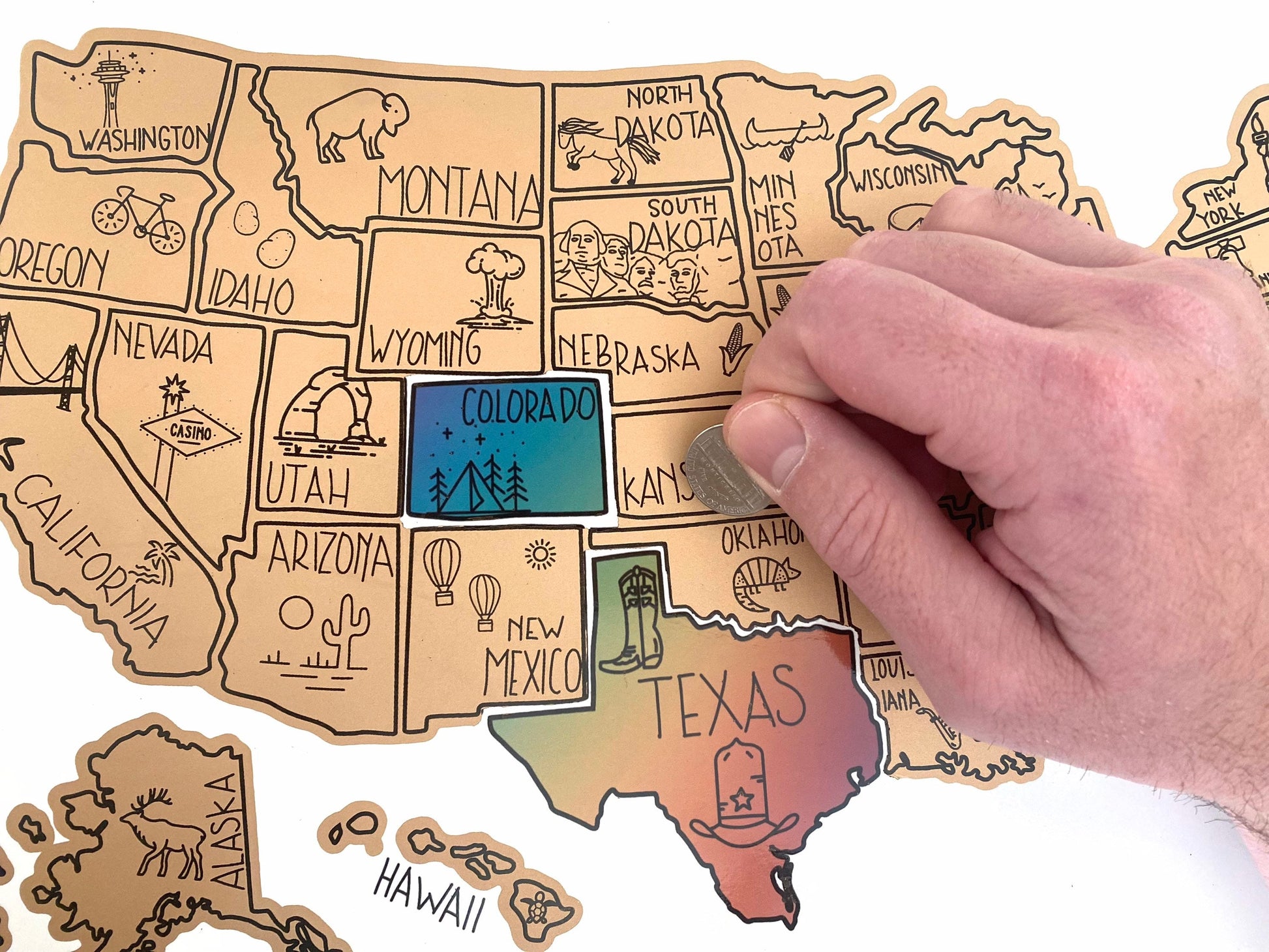 USA scratch off map. Has a white background. Scratch off a gold layer to reveal artwork underneath. Each state is represented by an icon and is colorful.  Hanging on a wooden frame.