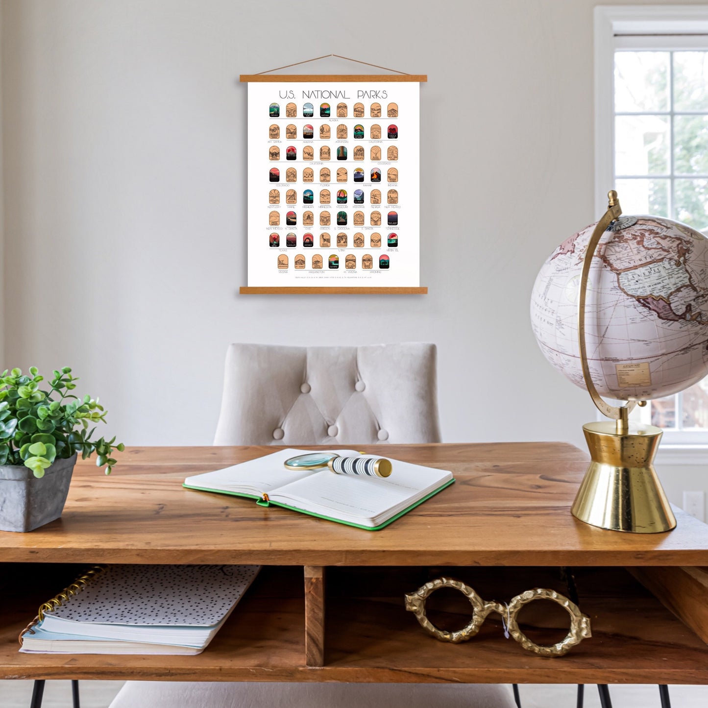 63 National Park scratch off poster, Has a black background with colorful icons for each park. Scratch off a gold layer to reveal artwork. Hanging on a wooden frame. Poster Hanging in an office.