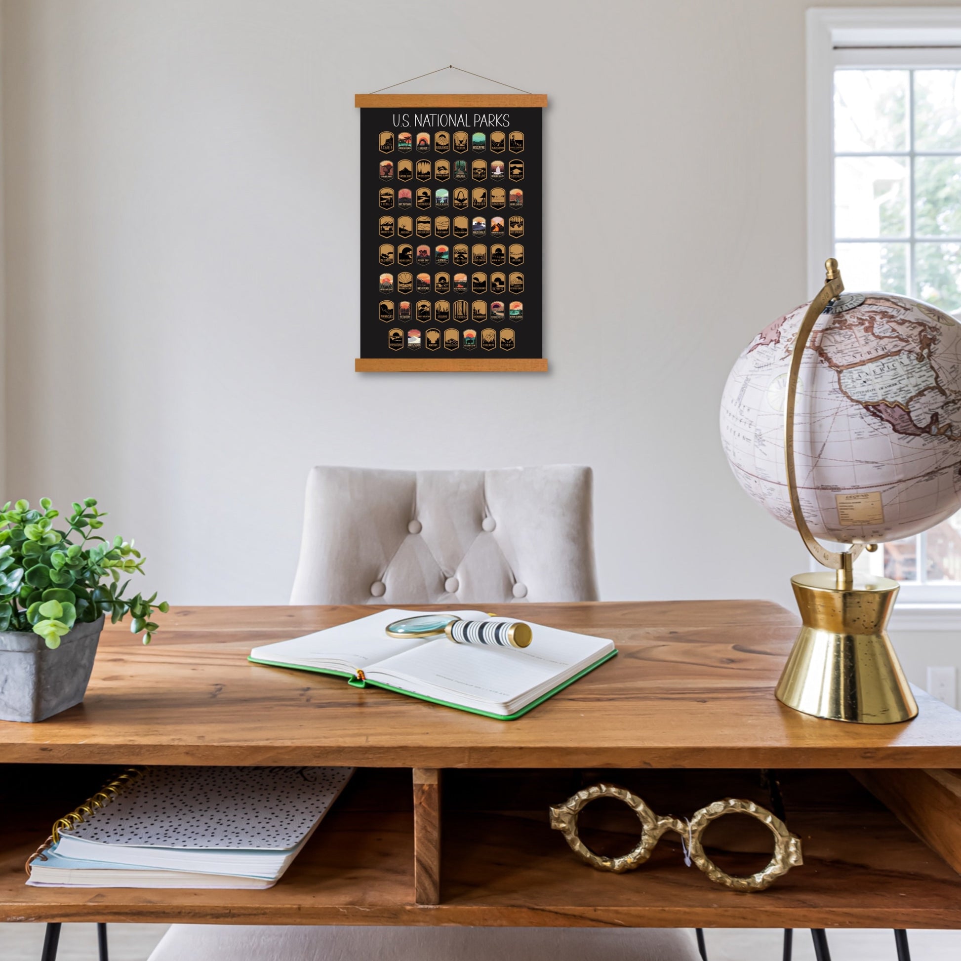 63 National Park scratch off poster, Has a black background with colorful icons for each park. Scratch off a silver layer to reveal artwork. Hanging on a wooden frame in an office.