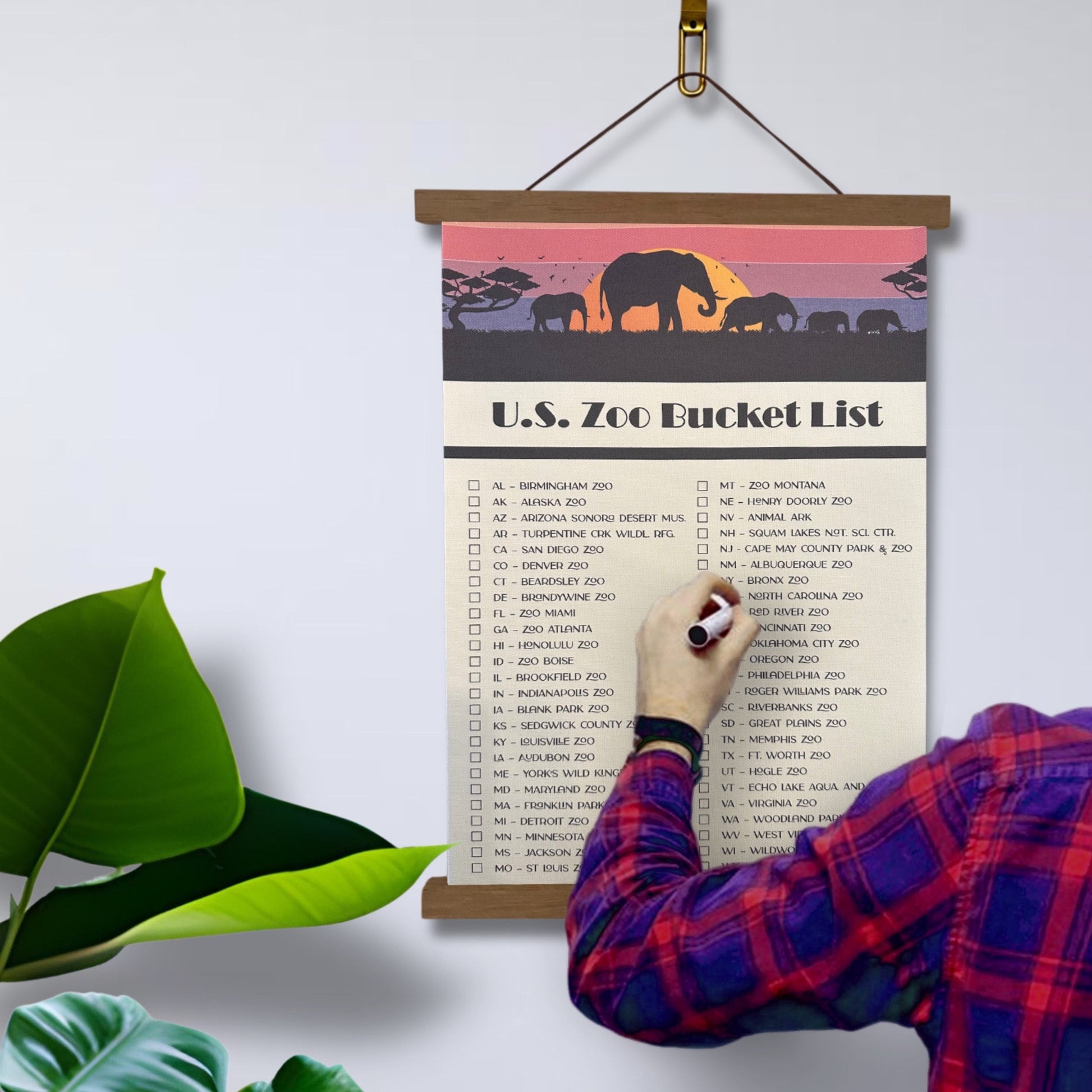 U.S. Zoo Bucket List Checklist Tracker with marker. Printed on canvas. Has a design on the top with a sunset and elephants. Hanging on a wooden frame.
