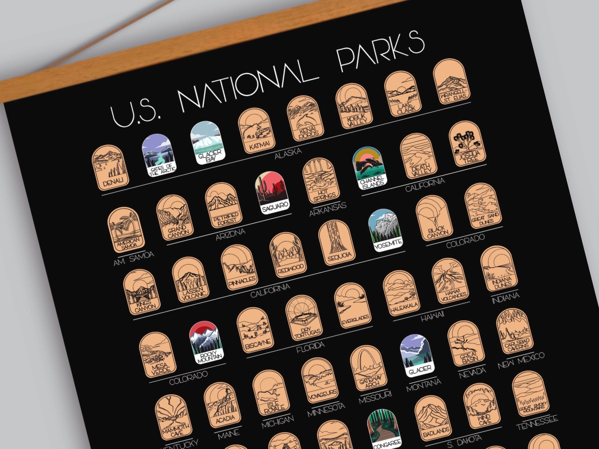 63 National Park scratch off poster, Has a black background with colorful icons for each park. Scratch off a gold layer to reveal artwork. Hanging on a wooden frame.