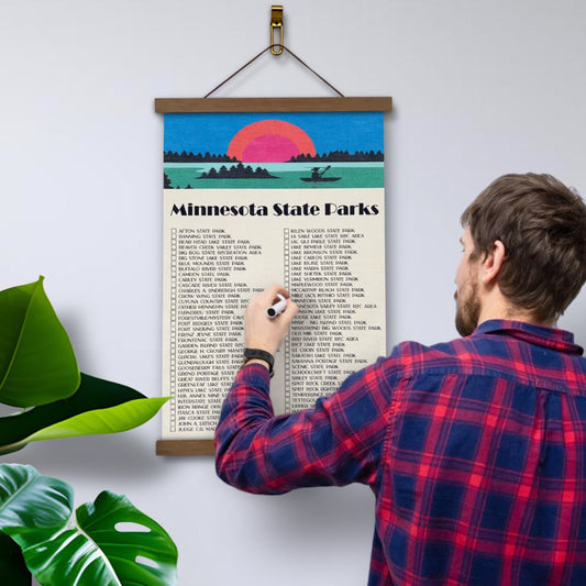 Minnesota State Parks Checklist Tracker. Printed on canvas. Has a design on the top with a sunset and canoe. Hanging on a wooden frame.